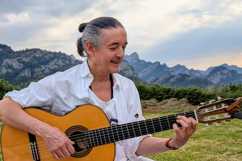 Manu tocando la guitarra al aire libre, con montañas detrás